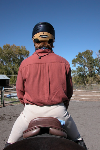 Photo 2. The rider has placed a folded washcloth underneath her right seat bone. Observe that now she is sitting level on the saddle. Her britches seam lines up with the center of the cantle. There is marked improvement in her alignment all the way up through her shoulders.